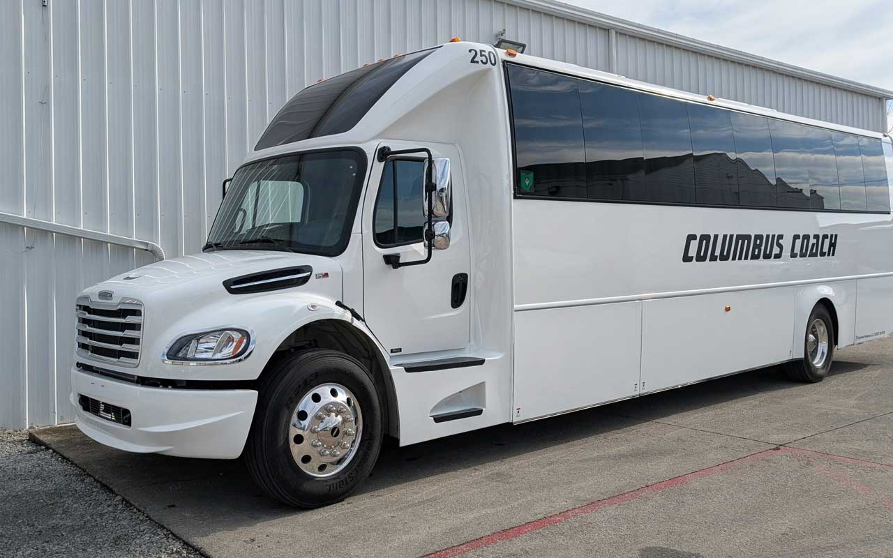 White 39-passenger Columbus Coach executive coach parked outside its facility.